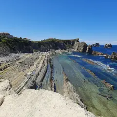 Espectacular vista de la playa de Arnia con sus formaciones rocosas y aguas cristalinas. Personas disfrutan del mar.