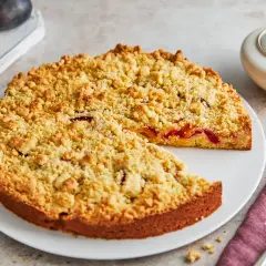 Ein saftiger Streuselkuchen mit Obst, bedeckt mit goldbraunen Streuseln, wartet darauf, angeschnitten zu werden.