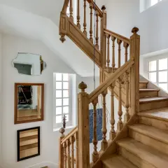 Un bel escalier en bois, prêt à être nettoyé. Des miroirs et des cadres photo décorent le mur blanc.