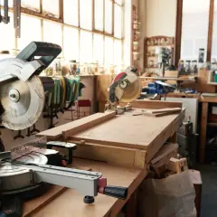 Un atelier menuiserie maison avec des scies circulaires, des établis et des outils. Des planches de bois sont prêtes pour être travaillées.
