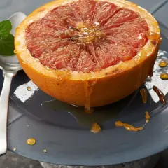 Halber Grapefruit mit Honig beträufelt, serviert auf einem Teller mit Minze. Ein köstliches, grapefruit low carb Frühstück.