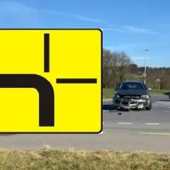 Znak drogowy informuje, kto ma pierwszeństwo na skrzyżowaniu równorzędnym. Widać uszkodzone auto po wypadku.