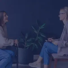 Terapeutka zajęciowa z notatnikiem rozmawia z pacjentką siedzącą na kanapie.