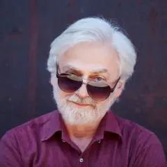 Krystian Zimerman w okularach przeciwsłonecznych, z siwą brodą i włosami, w bordowej koszuli.