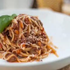 Pyszne spaghetti bolognese, klasyczny włoski przepis, z bogatym sosem mięsnym i parmezanem, ozdobione listkiem bazylii.