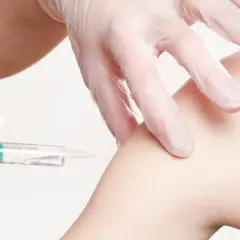 Ręka w rękawiczce medycznej podaje szczepionkę na wściekliznę przez igłę do ramienia.