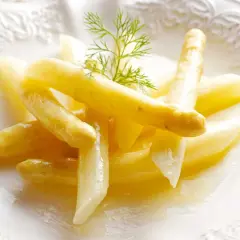 Espárragos blancos tiernos, cocidos y servidos en un plato blanco con una ramita de eneldo. Una guía visual para como cocer esparragos blancos.
