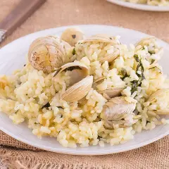 Un plato de arroz cremoso con almejas frescas, adornado con hierbas verdes. Un delicioso arroz con almejas listo para disfrutar.