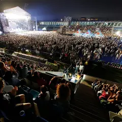 Multitud disfrutando de conciertos Torrelavega hoy. Escenario iluminado, miles de personas vibran con la música en un estadio.