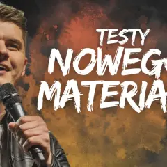 Uśmiechnięty komik na scenie, trzymający mikrofon. Na tle napis "TESTY NOWEGO MATERIAŁU".