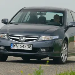 Ciemnoszary Honda Accord z kobietą za kierownicą jedzie po drodze.