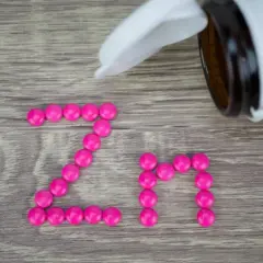 Różowe tabletki ułożone w napis "Zn" na drewnianym tle. Suplement cynku na co? Na odporność, skórę i włosy.