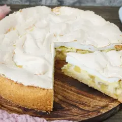 Ein saftiger Rhabarberkuchen mit Baiserhaube, ein Stück davon ist angeschnitten und zeigt die cremige Füllung.