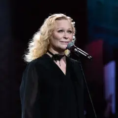 Blondynka w czarnej sukni śpiewa piosenkę aktorską przy mikrofonie.