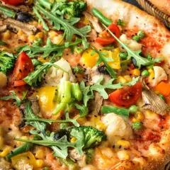 A pyszna pizza wegetariańska z brokułami, pomidorkami, kukurydzą i rukolą, posypana czarnym sezamem.