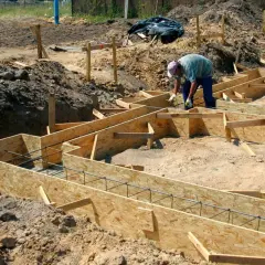 Budowa domu w toku: szalunek ławy fundamentowej zbrojony prętami, pracownik przygotowuje teren.