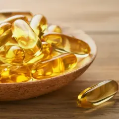 Goldene Kapseln auf einem Holzlöffel, die die positive Wirkung von Omega-3 auf die Psyche symbolisieren.