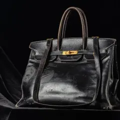 En svart, sliten läderväska i jane birkin style, med guldfärgade detaljer och initialerna J.B. präglade.