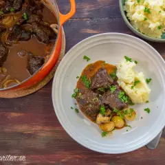 A Dutch oven filled with braised beef and mushrooms, next to a plate of beef with mashed potatoes and a bowl of mashed potatoes.