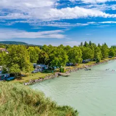 Słoneczny dzień na kempingu Balaton. Przyczepy kempingowe i namioty nad turkusową wodą, ludzie pływają i relaksują się.