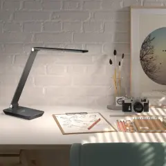 Flexo LED USB moderno sobre escritorio con cámara antigua, bocetos y arte.