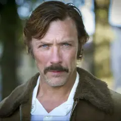 Porträtt av en svensk manlig skådespelare från Dramaten med mustasch och blå ögon, klädd i en brun jacka med foder.