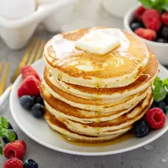 Pile de pancakes sans oeuf, dorés et moelleux, garnis de beurre fondant et de fruits rouges frais. Un délice pour le petit-déjeuner !