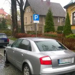 Samochody stoją na ulicy, a obok znak informuje o parkowaniu za przejściem dla pieszych.