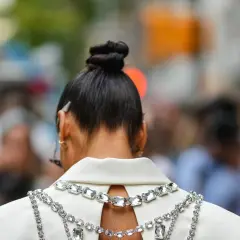 Capelli raccolti in un elegante chignon alto, impreziositi da una collana scintillante su un abito bianco.