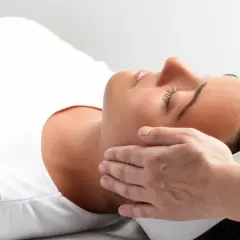 Kobieta w białej koszulce doświadcza relaksującego dotyku dłoni. To może być właśnie reiki co to za technika, która przynosi ukojenie.