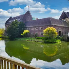 Schloss Wittringen, ein imposantes Backsteingebäude, spiegelt sich im Wasser eines umliegenden Grabens.