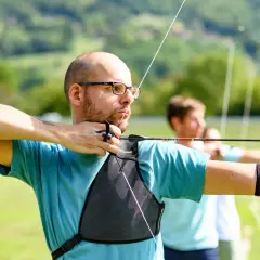 Łucznik napina łuk, skupiony na celu. Widać siłę naciągu łuku w jego postawie i napiętych mięśniach.