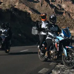 Motocykliści w kaskach jadący drogą wśród skalistych wzgórz.