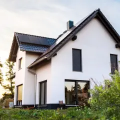 Nowoczesny biały dom z panelami słonecznymi na dachu, otoczony zielenią.