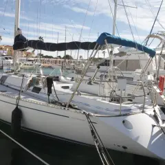Barche a vela ormeggiate in un porto, con la scritta "Genesi Sport" su una di esse. Cielo azzurro con nuvole.