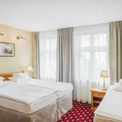 Pokój hotelowy z trzema łóżkami, idealny na wieczór panieński. Jasne ściany, zasłony i czerwony dywan tworzą przytulną atmosferę.