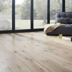 Un salon lumineux avec un parquet clair, une banquette grise et une vue sur un jardin verdoyant. Idéal pour peindre un parquet et créer une ambiance cosy.