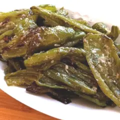 Friggitelli al forno, verdi e lucidi, conditi con sale e spezie, serviti su un piatto bianco.