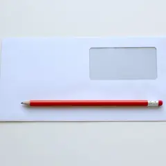 Biała koperta C5 z okienkiem i czerwony ołówek. Idealne wymiary do wysyłki dokumentów.