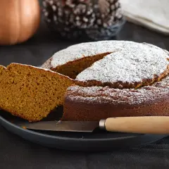 Un delicioso bizcocho de calabaza espolvoreado con azúcar glas, con una rebanada cortada y un cuchillo listo para servir.
