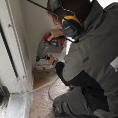 Mann bohrt Löcher für eine Bohrlochinjektion. Er trägt Gehörschutz und Arbeitskleidung.