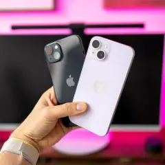 Dwa iPhone'y 14 w ręce, jeden ciemny, drugi fioletowy. Ich aparat jest gotowy do robienia zdjęć.