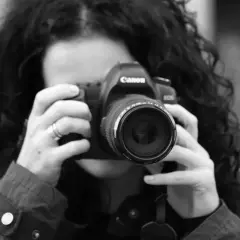 Kobieta z kręconymi włosami robi zdjęcie aparatem Canon. To jej pierwszy kurs na fotografa, uczy się łapać kadr.