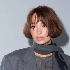Frau mit braunem, kurzem Bob mit Curtain Bangs, trägt grauen Blazer und Schal.