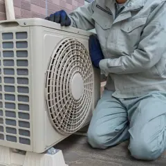 Pracownik w rękawiczkach sprawdza jednostkę zewnętrzną klimatyzacji. Wzór pozwolenia na montaż klimatyzacji w bloku jest kluczowy dla takich prac.