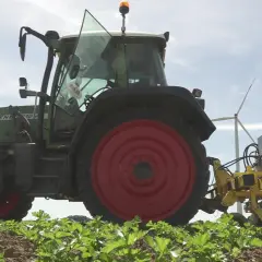 Ein grüner Traktor mit roter Felge arbeitet auf einem Feld. Die Maschine ist mit einem gelben Anbaugerät ausgestattet, das zeigt, wie wird Reis geerntet.