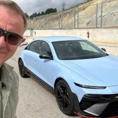 Mężczyzna w okularach przeciwsłonecznych pozuje do selfie z błękitnym Hyundaiem IONIQ 6 N na torze wyścigowym.