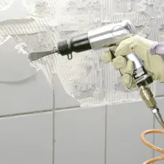 Mit einem Pressluftmeißel wird alter Fliesenkleber von der Wand entfernt.