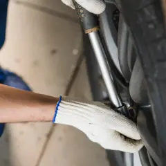 Mechanik w białej rękawicy dokręca śruby koła kluczem dynamometrycznym, dbając o odpowiednią siłę dokręcania kół w samochodzie.