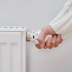 Mano ajustando el termostato de un radiador. El radiador solo calienta un lado, indicando un posible problema de circulación.